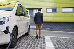 A man in business attire walking away from his car as he leaves it plugged in and charging.